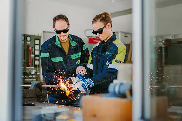 Ein Auszubildender zum Anlagenmechaniker (m/w/d) für Sanitär-, Heizungs- und Klimatechnik schweißt unter Anleitung seines Ausbilders in einer Werkstatt bei medl.