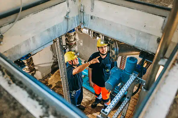 Ein Auszubildender zum Umwelttechnologen (m/w/d) für Rohrleitungsnetze und Industrieanlagen im Gespräch mit einem erfahrenen Kollegen in einem Pumpwerk der sem.